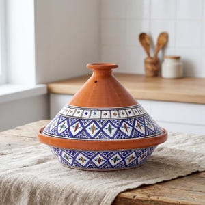 May include: A terracotta tagine cooking vessel featuring a conical lid and a wide base. The exterior is decorated with a blue and white diamond pattern, accented by small green, red, and yellow floral motifs. The top of the lid has a small knob.