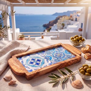 May include: A rectangular serving tray crafted from olive wood with two integrated handles. The center features two square ceramic tiles decorated with intricate blue and white floral patterns. The tray is positioned on a light-colored fabric.