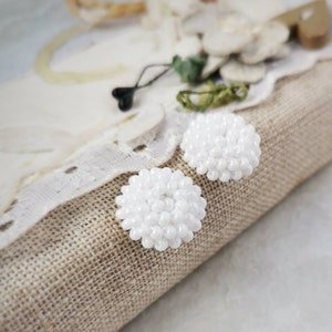 May include: A pair of white beaded earrings. The earrings are round and have a cluster of small white beads.