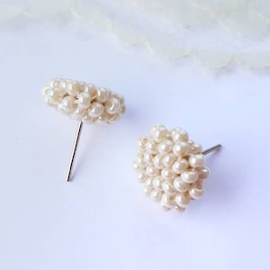 May include: A pair of small, white pearl earrings. The earrings are made of tiny white beads that are clustered together to form a round shape. The earrings are attached to silver posts.