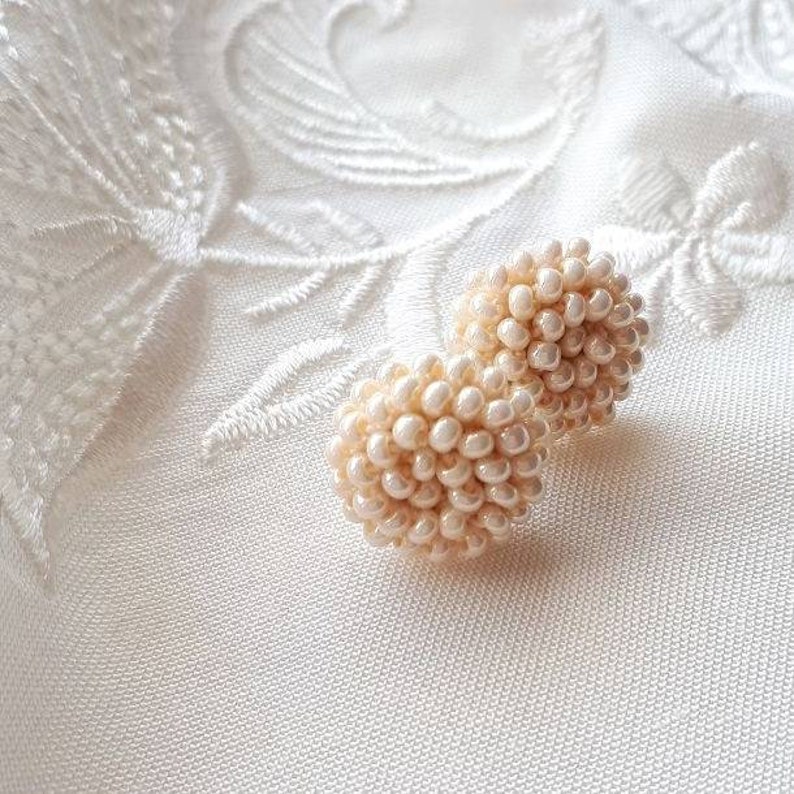 May include: Two small, round, cream-colored beaded earrings.