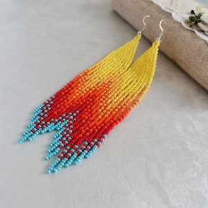 May include: A pair of long, beaded earrings with a gradient of yellow, orange, and red beads. The bottom of the earrings are finished with turquoise beads.