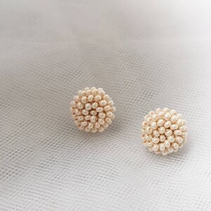 May include: A pair of cream-colored pearl bead earrings. The earrings are round and have a 3D design.