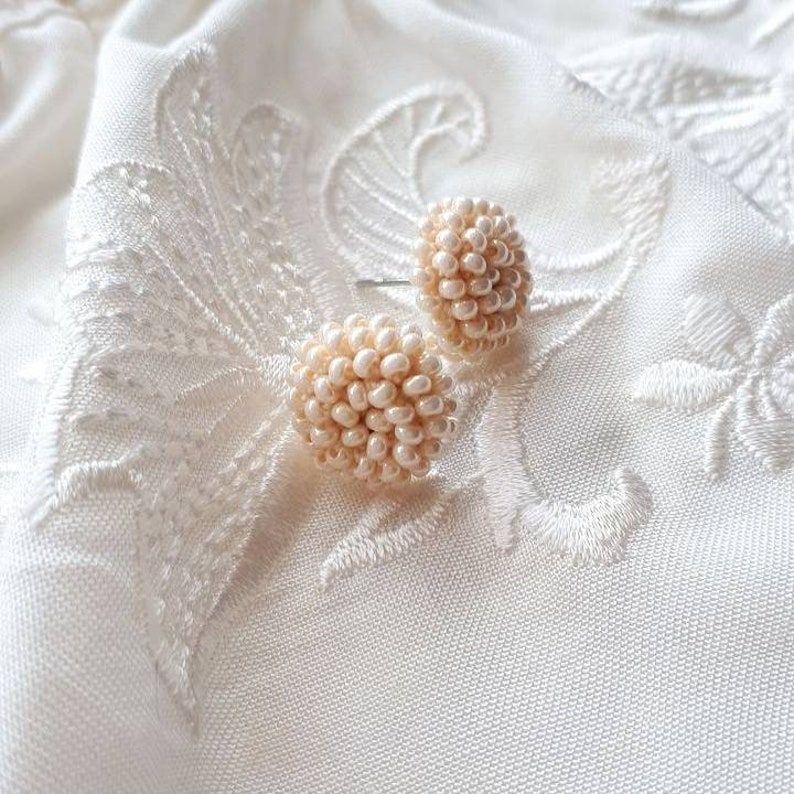 May include: A pair of cream-colored pearl beaded earrings. The earrings are round and have a delicate, feminine look.