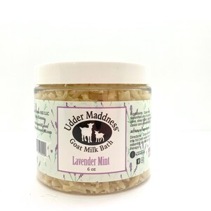 Puede incluir: Un tarro blanco con una etiqueta transparente que dice "Udder Madness Goat Milk Bath" y "Lavender Mint" con una imagen de dos cabras. El tarro está lleno de virutas blancas de jabón de baño de leche de cabra. El tarro es de 6 oz.
