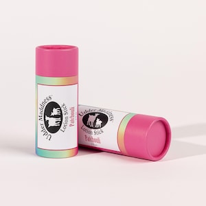 May include: Two pink lotion sticks with the text "Udder Maddness Lotion Stick Patchouli" and a logo of a cow and calf. One stick is upright, the other is lying down. The labels have a rainbow gradient.