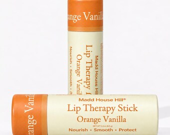 May include: Two cylindrical lip therapy sticks with orange caps and cream-colored labels. The text reads Madd House Hill Lip Therapy Stick Orange Vanilla, Nourish, Smooth, Protect, and Net Wt 0.3 oz (8.5 g). One stick stands upright, while the other lies horizontally.