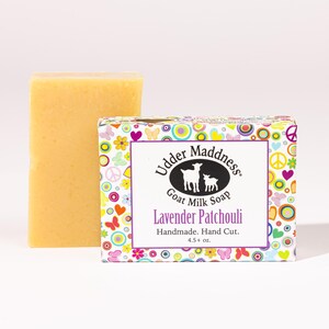 Peut inclure: Un pain rectangulaire de savon au lait de chèvre jaune à côté de son emballage. L'étiquette présente un ovale noir avec deux silhouettes de chèvres blanches, le texte Udder Maddness Goat Milk Soap, Lavender Patchouli et une bordure colorée.