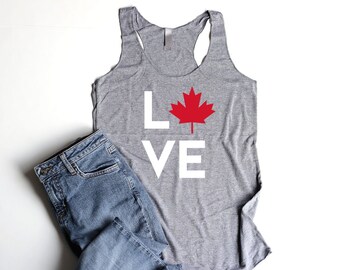 May include: Gray tank top with a white "LOVE" graphic and a red maple leaf in the center. The tank top is paired with blue jeans.