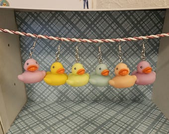 May include: Five pairs of rubber ducky earrings in pastel colors: pink, yellow, light yellow, light blue, and peach. The earrings are hanging from a string.