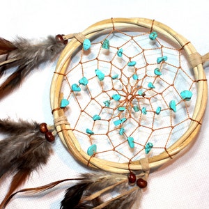 Peut inclure: Un attrape-rêves en bois brun avec une toile turquoise et cuivre et des plumes. L'attrape-rêves a une frange perlée.