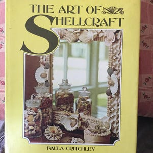 May include: A yellow book titled "The Art of Shellcraft" with a large letter "S" on the cover. The book features a photo of a mirror frame and jars decorated with seashells.