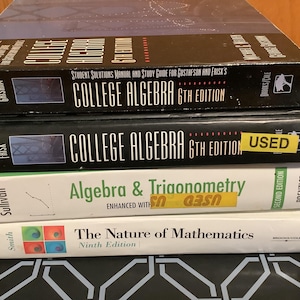 May include: A stack of four textbooks. The top book is titled "College Algebra 6th Edition". Below it is another "College Algebra 6th Edition" book with a "USED" sticker. The other books are "Algebra & Trigonometry" and "The Nature of Mathematics".