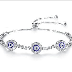 Könnte beinhalten: Silberarmband mit drei blauen bösen Augen-Anhängern, die jeweils von klaren Zirkonia-Steinen umgeben sind. Das Armband hat einen verstellbaren Schiebeverschluss.