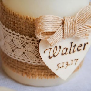May include: A white candle with a burlap and lace ribbon, a burlap bow, and a wooden heart tag with the name "Walter" and the date "5.13.17" written on it.