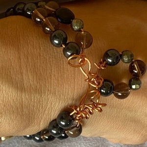May include: A multi-strand bracelet with brown, black, and gold beads. The bracelet is made with copper wire and has a clasp.