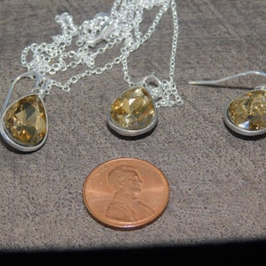 May include: A set of teardrop-shaped earrings and a matching necklace with clear amber-colored crystals. The jewelry is made of silver and has a delicate design.