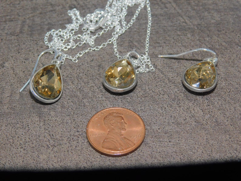 May include: A set of teardrop-shaped earrings and a matching necklace with clear amber-colored crystals. The jewelry is made of silver and has a delicate design.