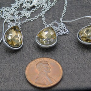 May include: A set of teardrop-shaped earrings and a matching necklace with a silver chain and clear amber-colored crystal stones.