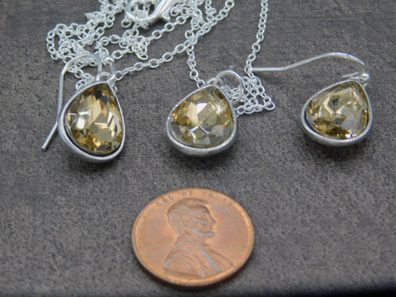 May include: A set of teardrop-shaped earrings and a matching necklace with a silver chain and clear amber-colored crystal stones.