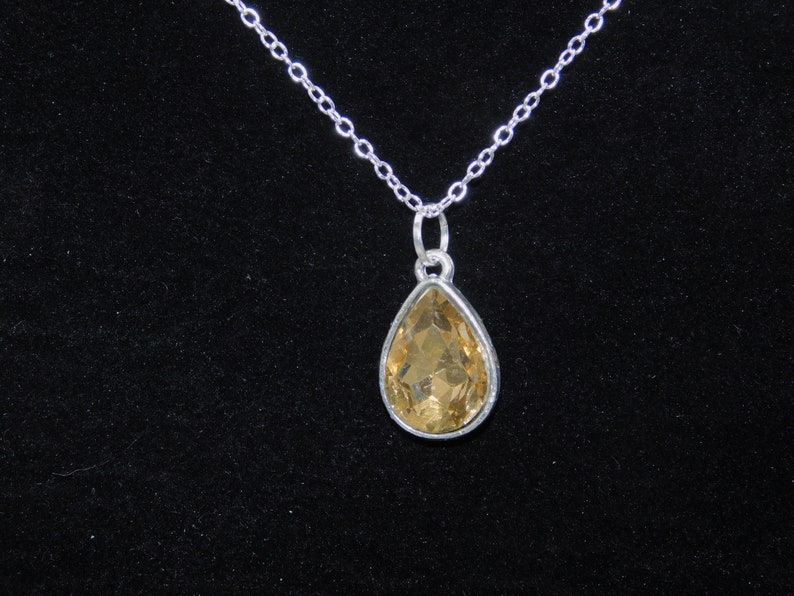 May include: A silver chain necklace with a teardrop-shaped pendant featuring a clear, amber-colored gemstone.