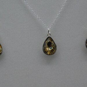 May include: A gold teardrop pendant necklace and matching earrings. The pendant and earrings are set with clear faceted stones.