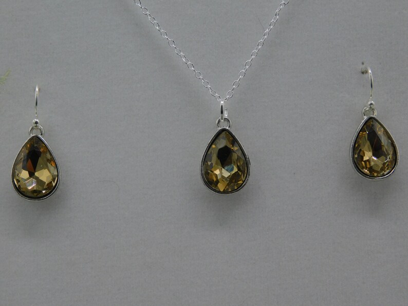 May include: A gold teardrop pendant necklace and matching earrings. The pendant and earrings are set with clear faceted stones.