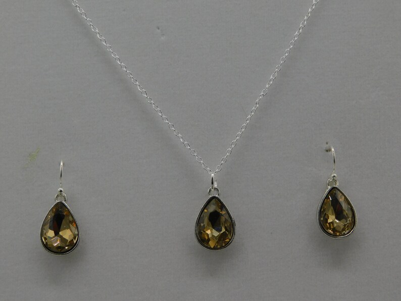 May include: A silver necklace and earrings set with teardrop-shaped amber-colored crystals.