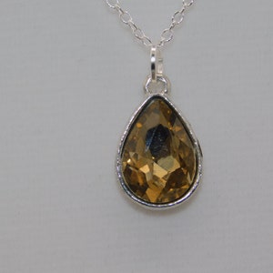 May include: A silver chain necklace with a teardrop-shaped pendant featuring a large, faceted, amber-colored crystal.