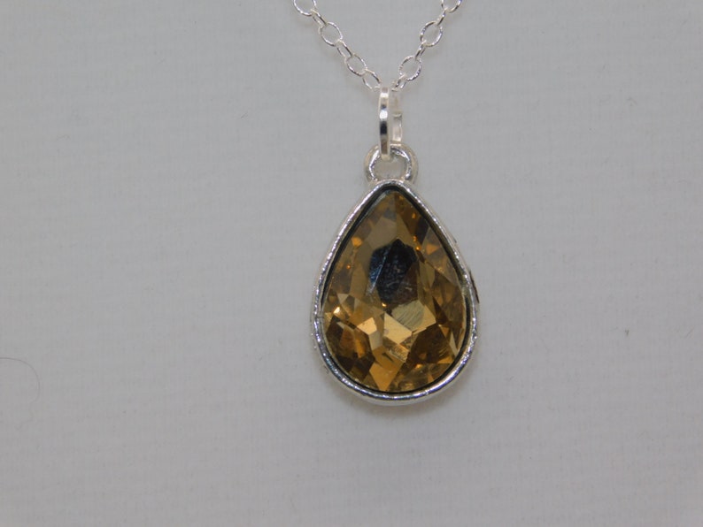 May include: A silver chain necklace with a teardrop-shaped pendant featuring a large, faceted, amber-colored crystal.