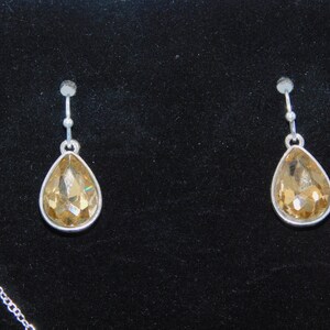 May include: A pair of silver dangle earrings with teardrop-shaped amber crystals.