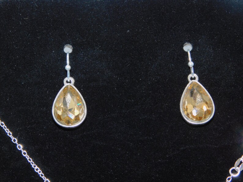 May include: A pair of silver dangle earrings with teardrop-shaped amber crystals.