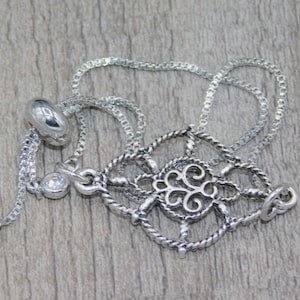 May include: A silver chain bracelet with a silver filigree charm and clear crystal accents.