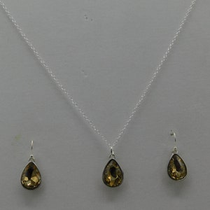 May include: A silver necklace with a teardrop-shaped pendant and matching earrings. The pendant and earrings feature a clear, amber-colored gemstone.
