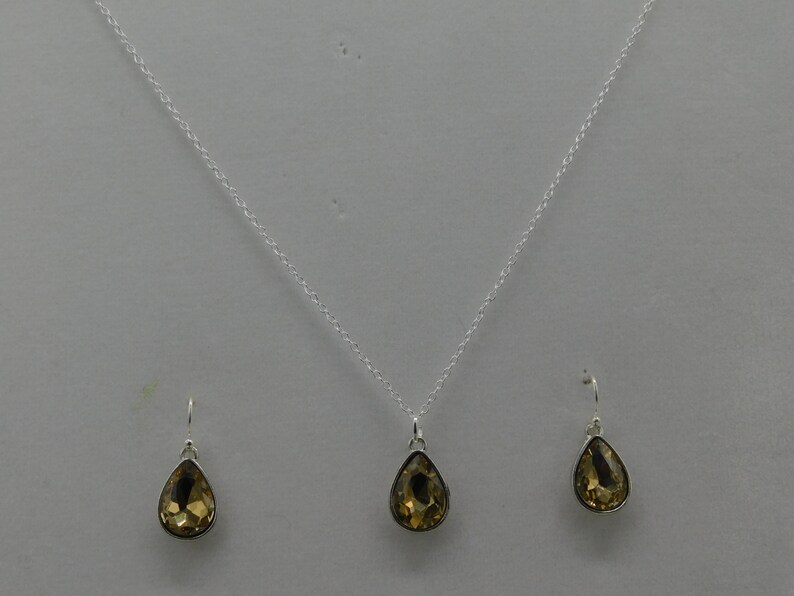 May include: A silver necklace with a teardrop-shaped pendant and matching earrings. The pendant and earrings feature a clear, amber-colored gemstone.
