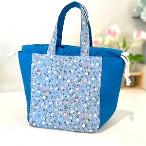 May include: A blue tote bag with a floral print on one side and solid blue on the other. The bag has a drawstring closure and two handles.