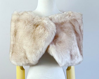May include: A beige faux fur shawl draped over a white mannequin. The shawl is soft and fluffy, and it would be perfect for a special occasion.