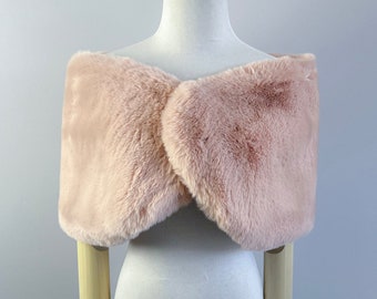 May include: A soft, blush pink faux fur shawl. The shawl is draped over a white mannequin with wooden arms.