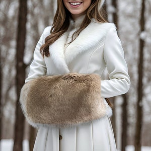 Pode incluir: Um casaco de inverno branco com gola e punhos de pele. O casaco tem um capuz forrado de pele e fecho de botões. A modelo está usando o casaco em um cenário de floresta nevada.