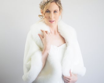 May include: A white faux fur shawl with a long white dress and a gold and pearl headband.