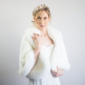 May include: A white faux fur shawl with a long white dress and a gold and pearl headband.