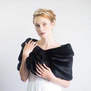 May include: A woman wearing a white dress with a black faux fur shawl. She is wearing a gold headband with feathers.