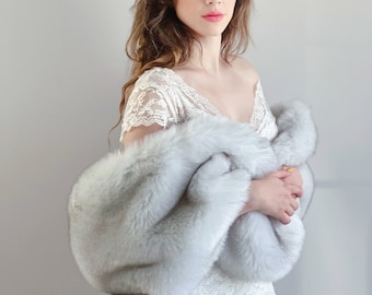 May include: A woman wearing a white lace dress with a faux fur shawl. She is wearing a gold leaf crown and has her hair down.