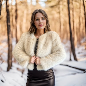 May include: A woman wearing a white faux fur jacket over a black dress, standing in a snowy forest.