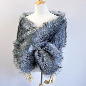 May include: A gray faux fur shawl with a soft, fluffy texture. The shawl is draped over a mannequin and is perfect for adding a touch of warmth and elegance to any outfit.