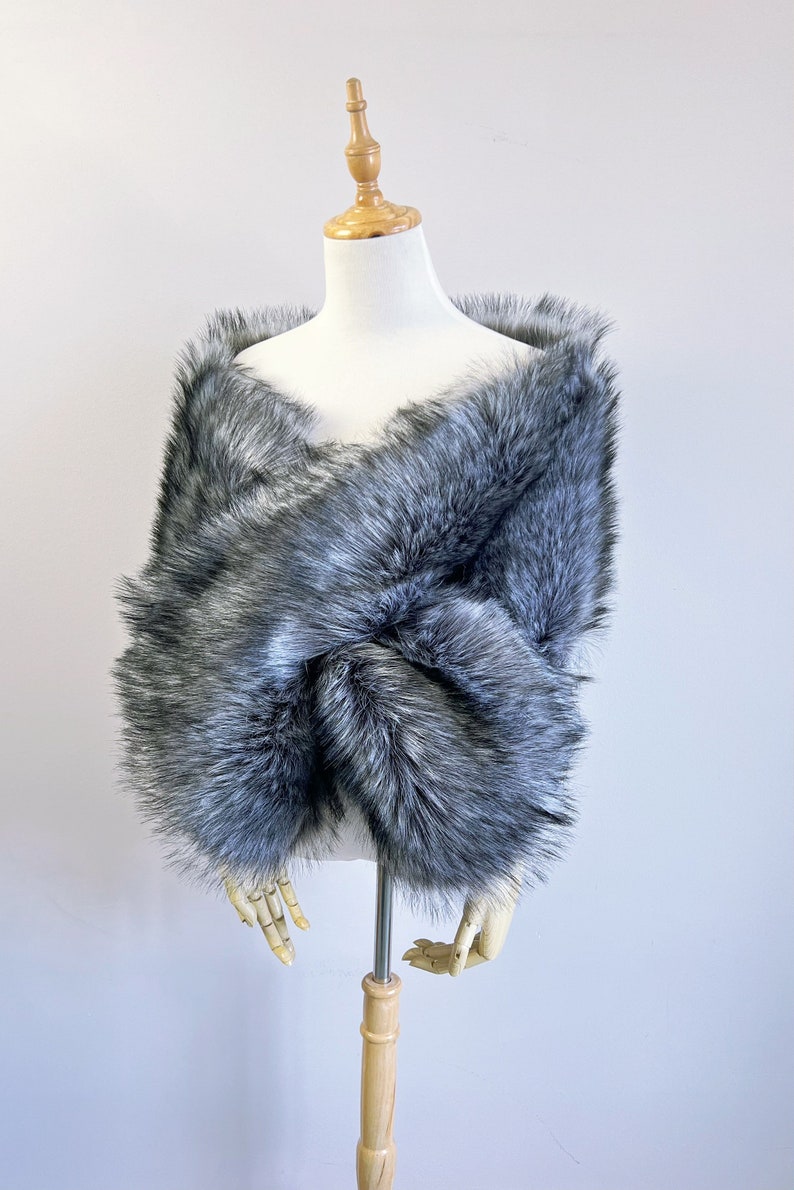 May include: A gray faux fur shawl with a soft, fluffy texture. The shawl is draped over a mannequin and is perfect for adding a touch of warmth and elegance to any outfit.