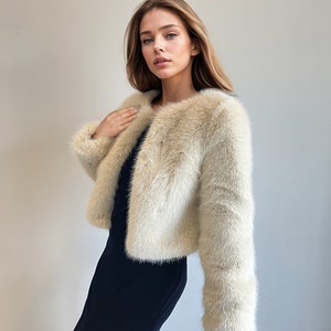 May include: A cream-colored faux fur jacket with a cropped length and long sleeves. The jacket is made of soft, fluffy fur and has a simple, elegant design.