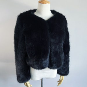 May include: A black faux fur cropped jacket with a v-neckline.