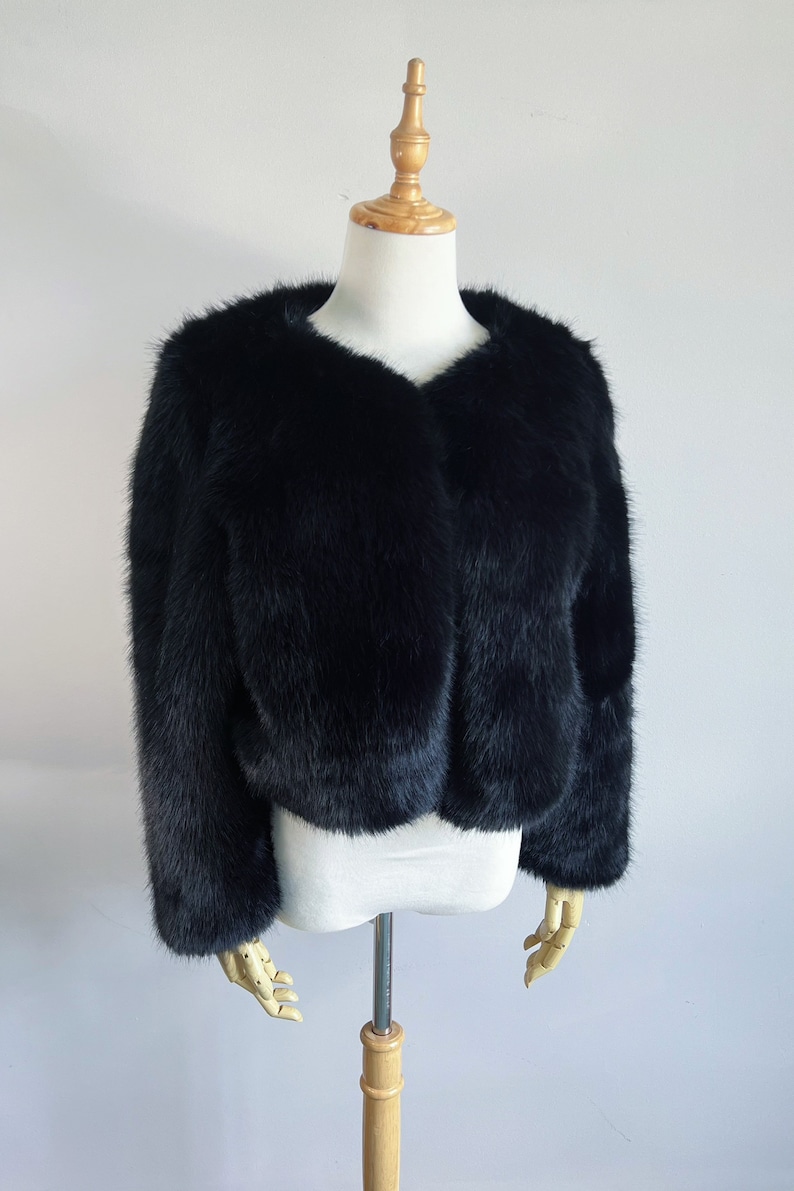 May include: A black faux fur cropped jacket with a v-neckline.