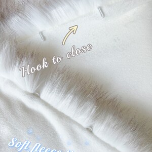 May include: White faux fur hooded scarf with a soft fleece lining. The scarf has two hooks on the inside to close the hood.